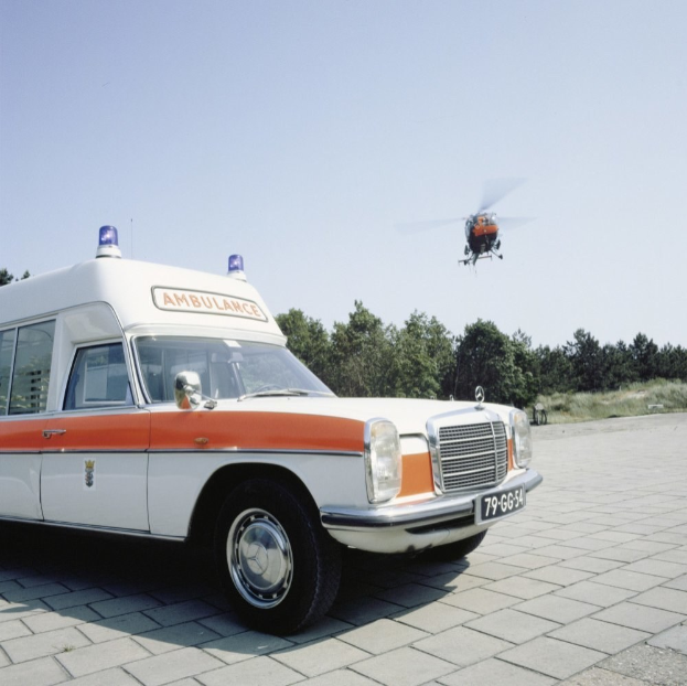 Ambulanz vor einem Hubschrauber mit Bäumen und einem klaren blauen Himmel im Hintergrund.