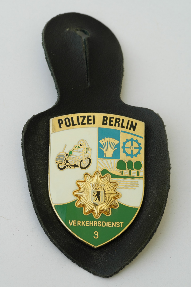 Polizei Berlin Abzeichen mit einem blauen Schild, einem weißen Stern und schwarzem Text auf einem weißen Rand, das auf einer Oberfläche platziert ist.