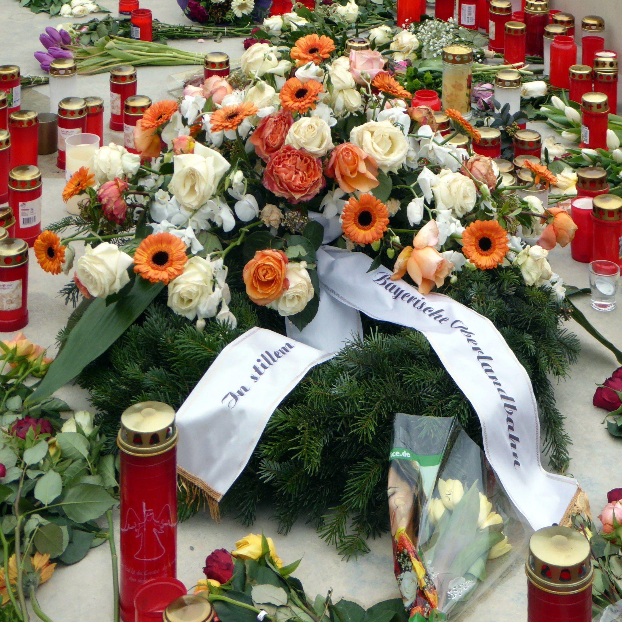 Memorial in Berlin with flowers and candles placed on the ground in front of a wall.