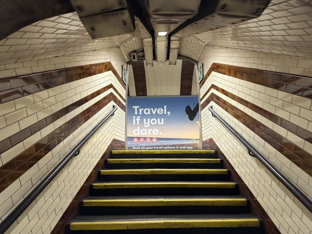 Eine U-Bahn-Stationstreppe mit Geländern auf beiden Seiten, die ein "Reise, wenn du wagst"-Schild oben und sichtbare Stationswände im Hintergrund zeigt.