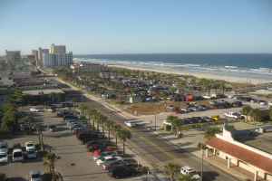 Fahrzeuge sind in der Nähe von Bäumen, Gebäuden und einem Ozean geparkt.