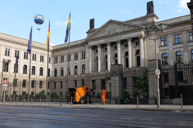 Large modern government building with many windows, surrounded by street furniture and vehicles, with the German Bundestag flag visible.