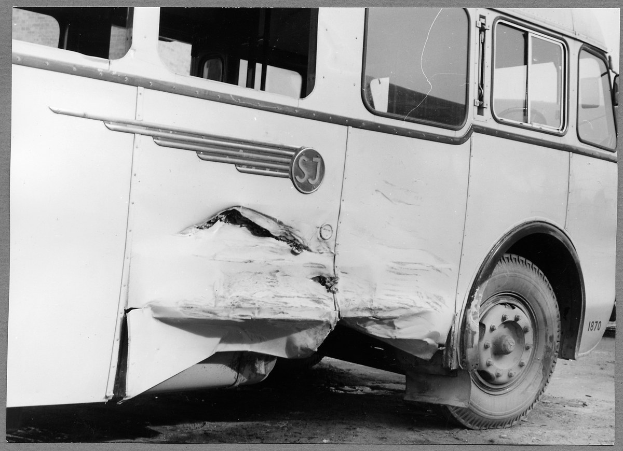 Schwarzes und weißes Foto eines verbeulten Busses mit zersplitterten Fenstern und offener Fahrertür, die das beschädigte Innere zeigt.