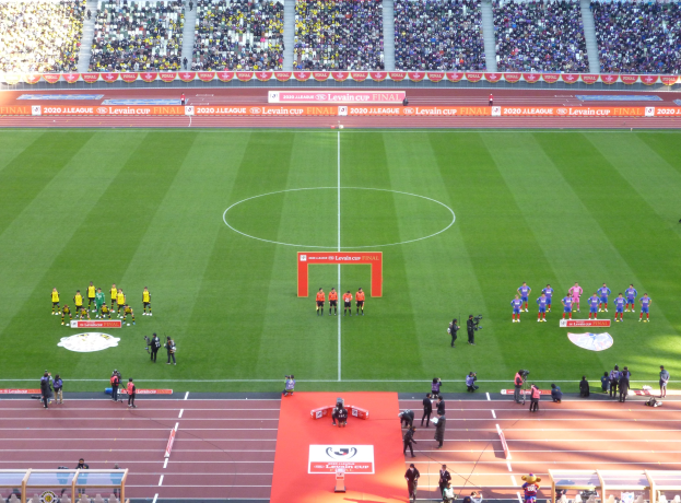 Eine Gruppe von Menschen steht auf einem grünen Fußballfeld in einem Stadion voller Zuschauer, mit Werbetafeln für das Levin-Cup-Finale 2020 rund um das Feld.