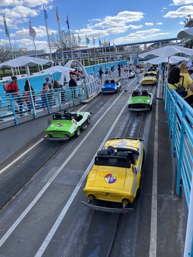 Gruppe von Menschen, die eine Achterbahn in Disney's Hollywood Studios fahren, umgeben von Geländern und Fahnen, mit Bäumen und Gebäuden im Hintergrund unter einem bewölkten Himmel.