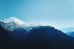 Ein majestätischer Blick auf den Annapurna-Basis-Camp-Trek in Nepal, mit schneebedeckten Bergen im Vordergrund und einem klaren blauen Himmel im Hintergrund.