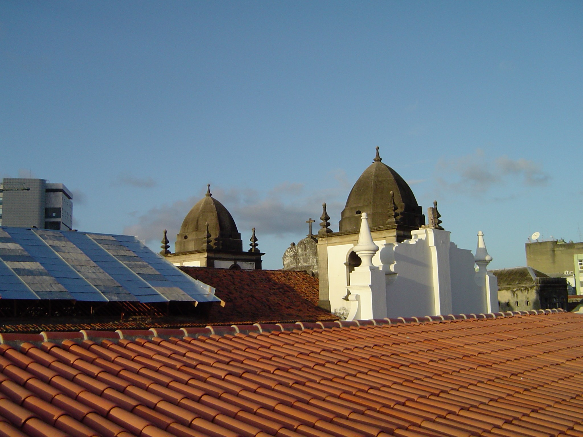 Stadtpanorama mit Gebäuden im Vordergrund und einem blauen Himmel im Hintergrund, mit Solarpanelen auf einem Dach, die erneuerbare Energie nutzen.