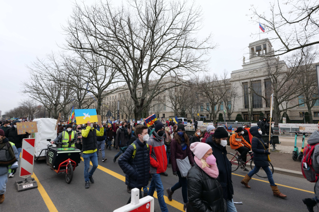 Eine große Gruppe von Menschen nimmt an einer Protestdemo in Washington, D.C. am 21. Januar 2020 teil und marschiert eine Straße entlang mit Schildern, Bannern und Fahrrädern vor einer Kulisse aus Schildern, Bäumen und einem klaren blauen Himmel.