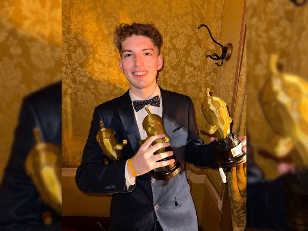 Ein Mann im Smoking hält eine Oscar-Statue und strahlt gegen eine Wand, was darauf hinweist, dass er den Oscar für den besten Nebendarsteller gewonnen hat.